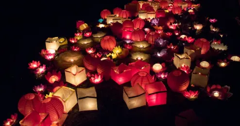 一張會安燈籠節期間的照片，彩色燈籠隨水漂流於秋盆河上，河岸點綴著燈光與人群，營造出溫馨而浪漫的節慶氛圍