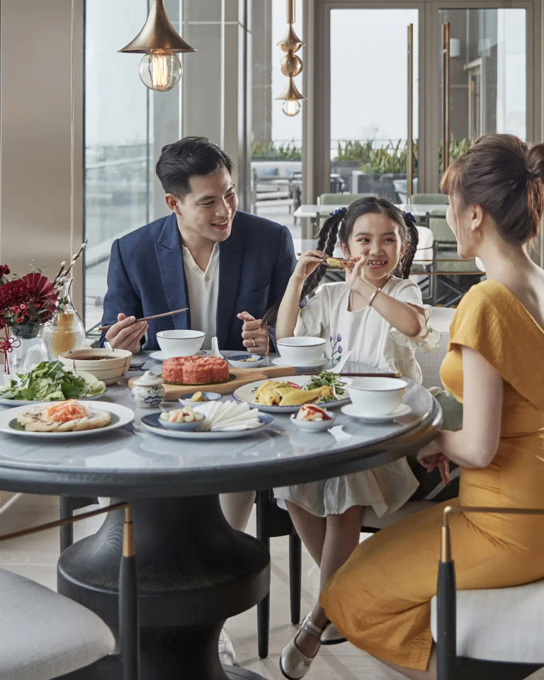 一張家庭用餐照片，展示一家人在會安西式餐廳裡共享披薩與義大利麵，氣氛溫馨歡樂，餐廳裝潢充滿歐式風格